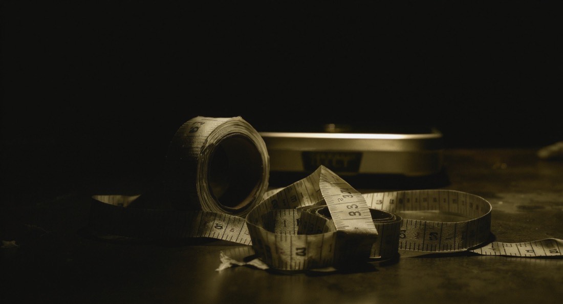 A cloth tape measure and bathroom scale on a dark floor