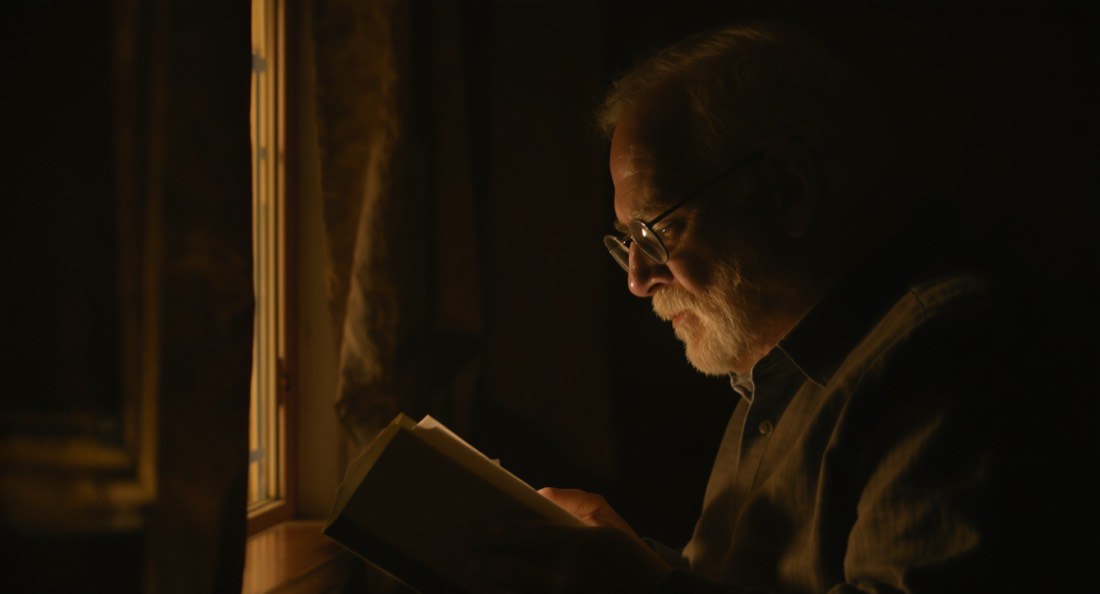 An older man reading in profile in warm window light