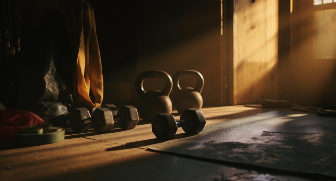 A home garage gym corner with adjustable dumbbells, a kettlebell, a band and a mat