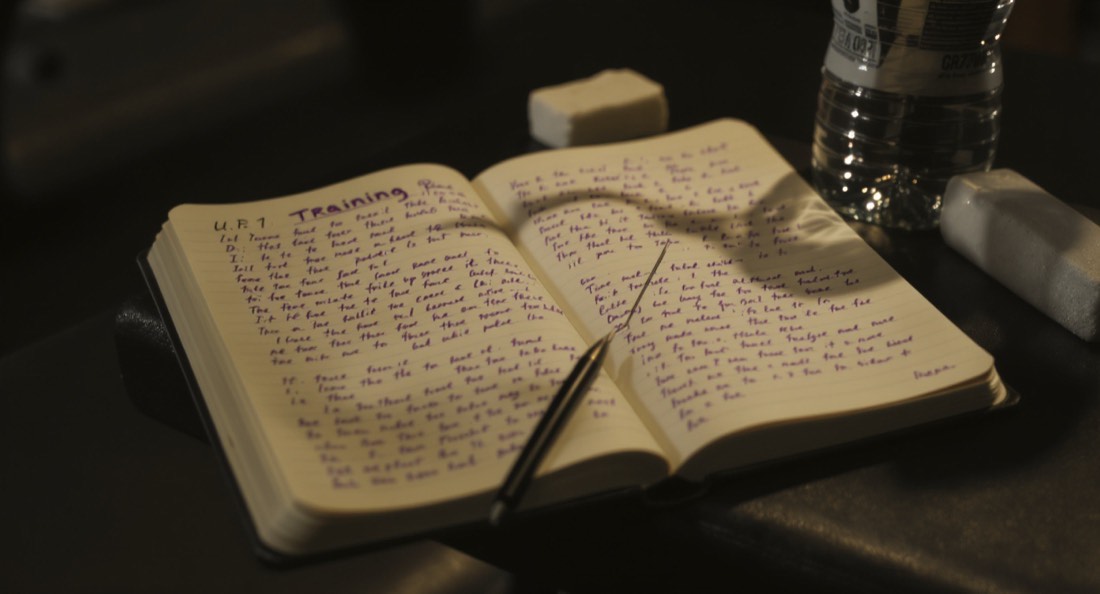 An open training notebook on a gym bench beside a water bottle and chalk