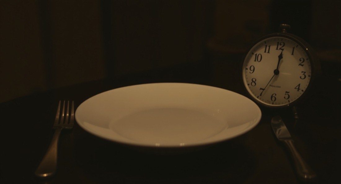 An empty plate with cutlery beside an analogue wall clock
