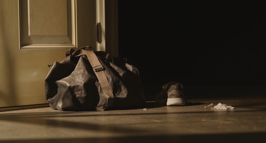 A worn gym bag and training shoes by a front door in early morning light