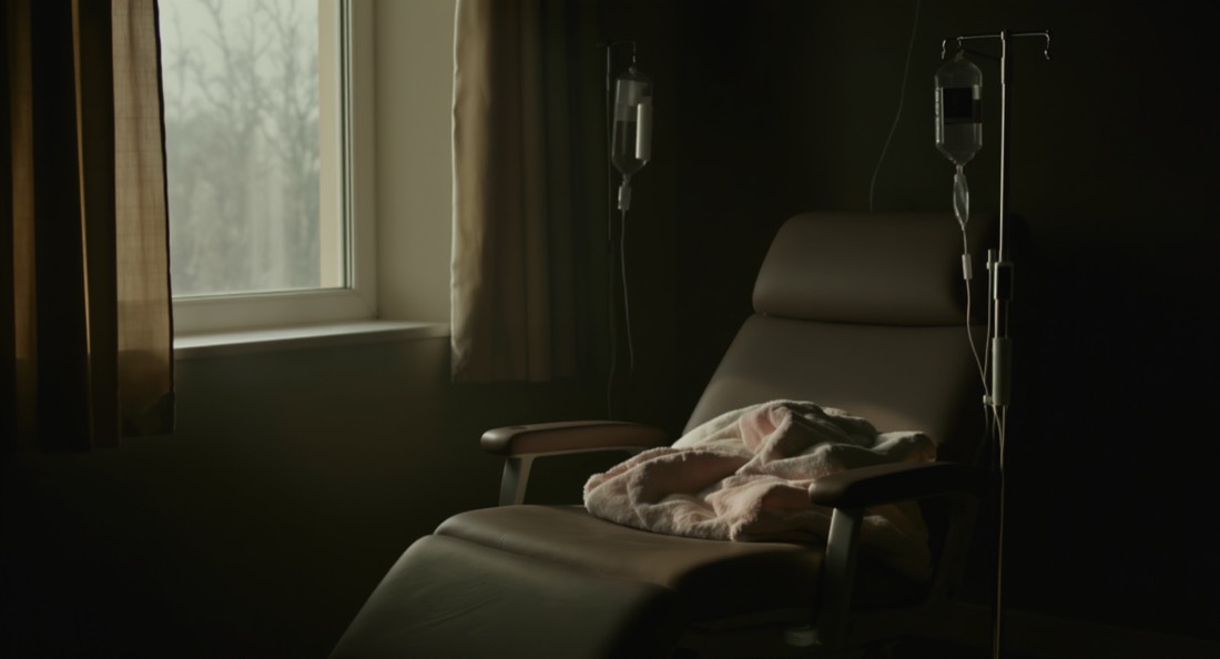 An empty clinic infusion chair beside a window with an IV stand
