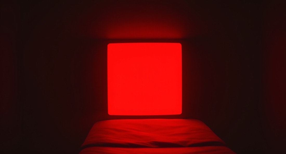 A large red light therapy panel glowing in a dark treatment room