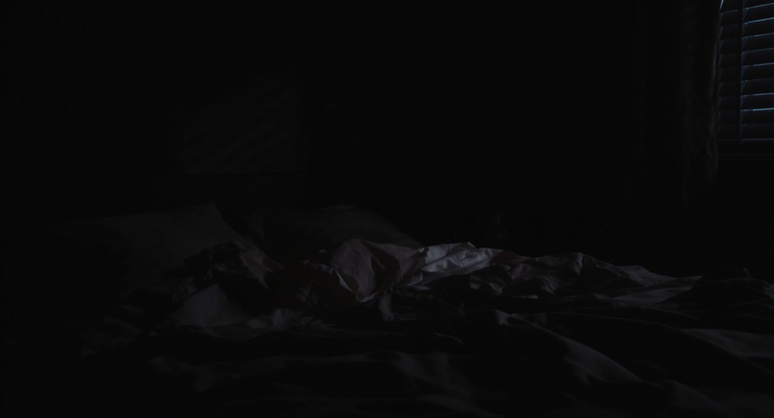 A dark quiet bedroom before dawn with light through slatted blinds