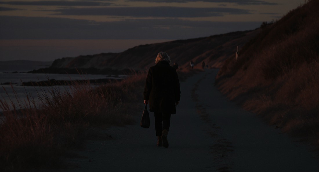 A woman in her fifties walking alone on a coastal path at dusk